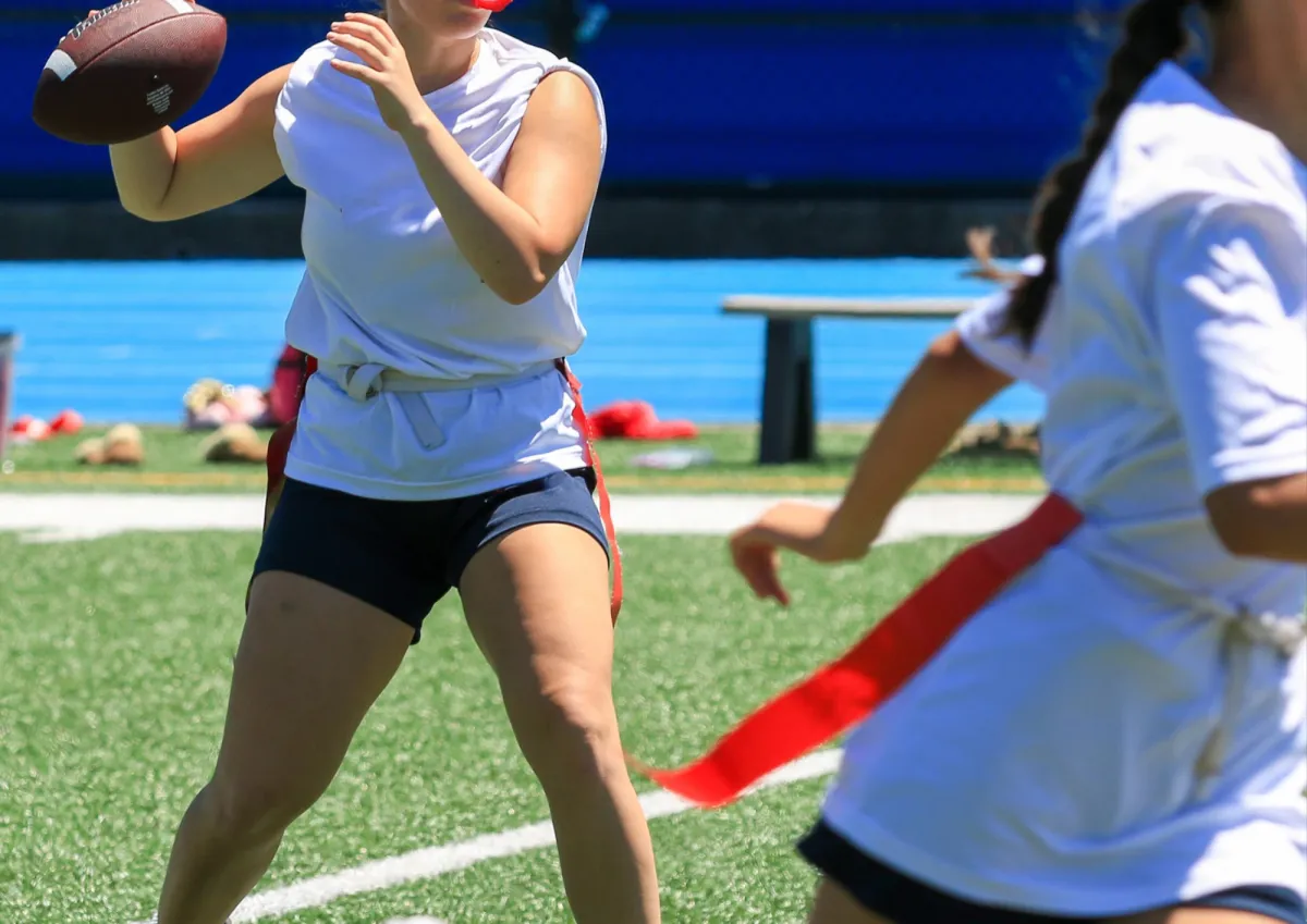 qué es el tocho bandera: quarterback a punto de lanzar mientras una defensora con cinturón de banderas corre hacia ella